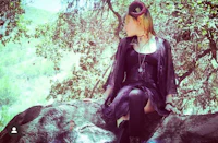 a woman in a black dress sitting on a rock