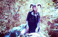 a woman with horns sitting on a rock in the woods
