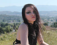 a woman with long black hair sitting on top of a hill