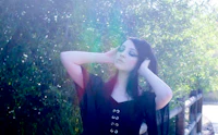 a woman in a black dress leaning against a fence